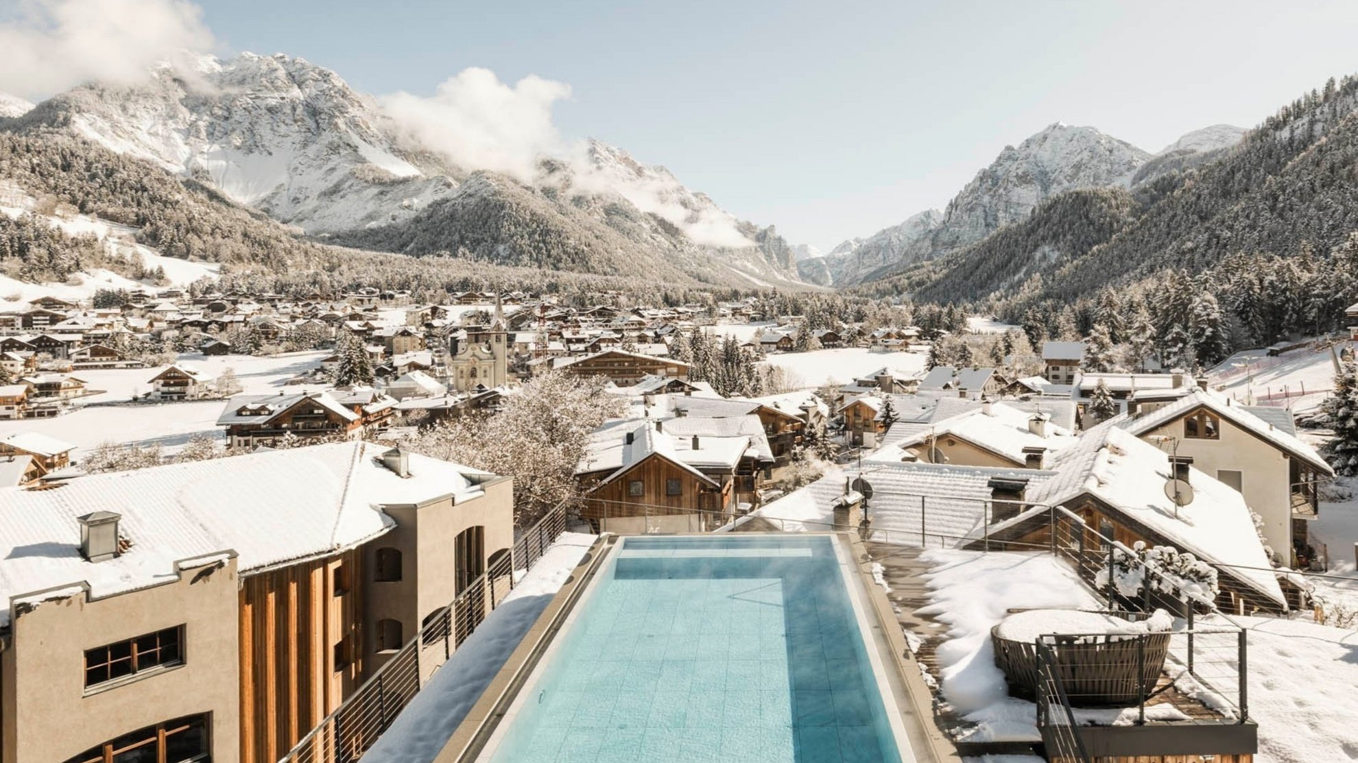 Hotel in South Tyrol with guided hikes Mountain village with snow-covered houses and rooftop pool in winter