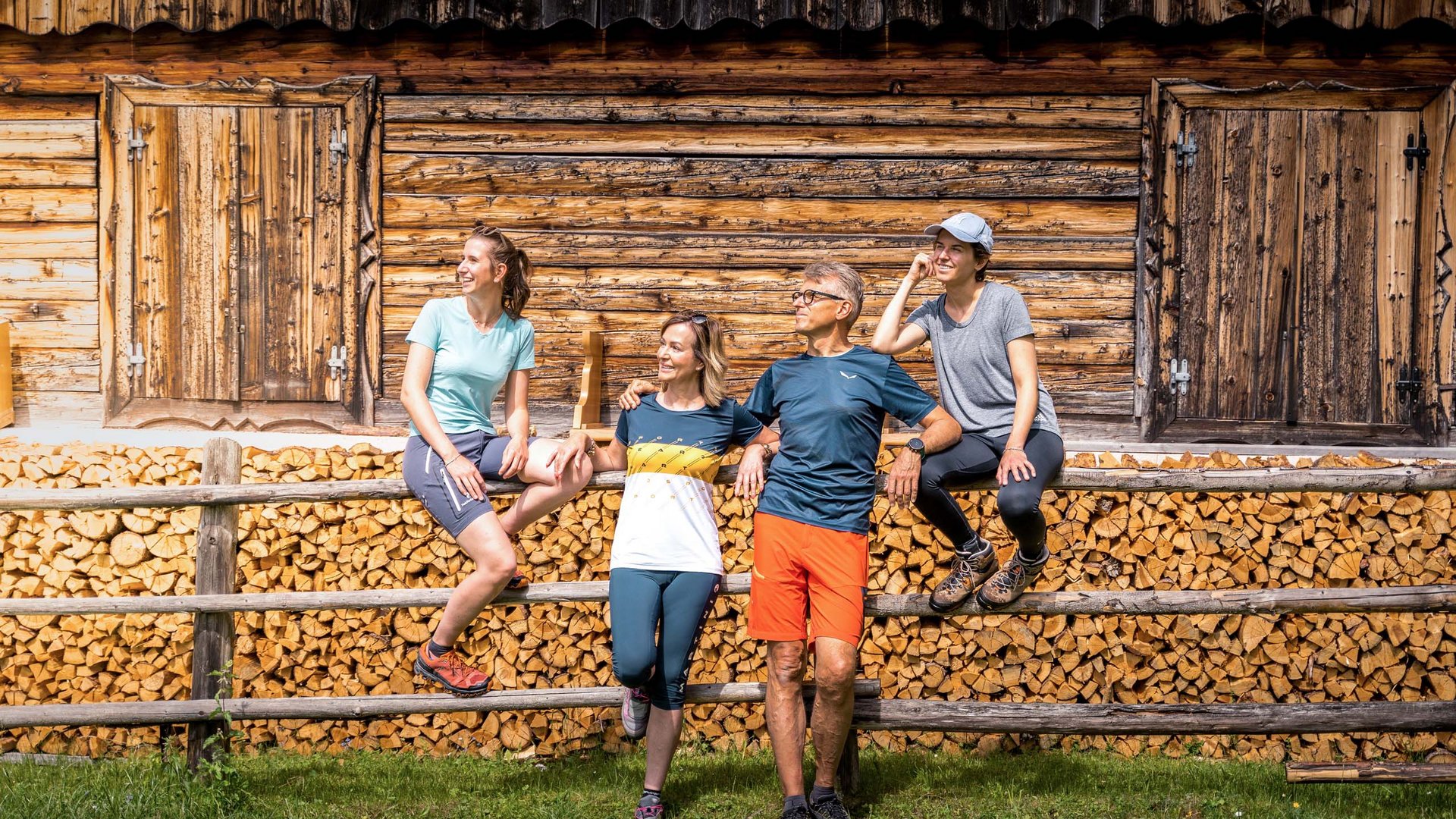 Dolomiten-Hotel für Bergmenschen Vier Wanderer lehnen entspannt an einem Holzstapel vor einer Berghütte
