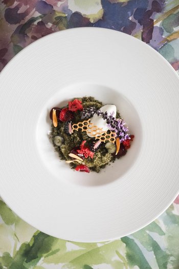 Das Gourmethotel in Südtirol Fein garniertes Gourmetgericht auf einem weißen Teller mit Blumenmuster im Hintergrund