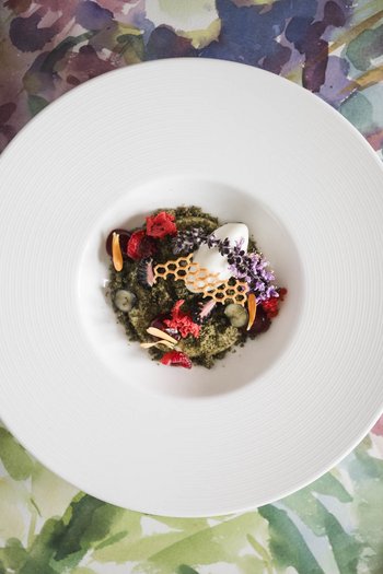 Das Gourmethotel in Südtirol Fein garniertes Gourmetgericht auf einem weißen Teller mit Blumenmuster im Hintergrund