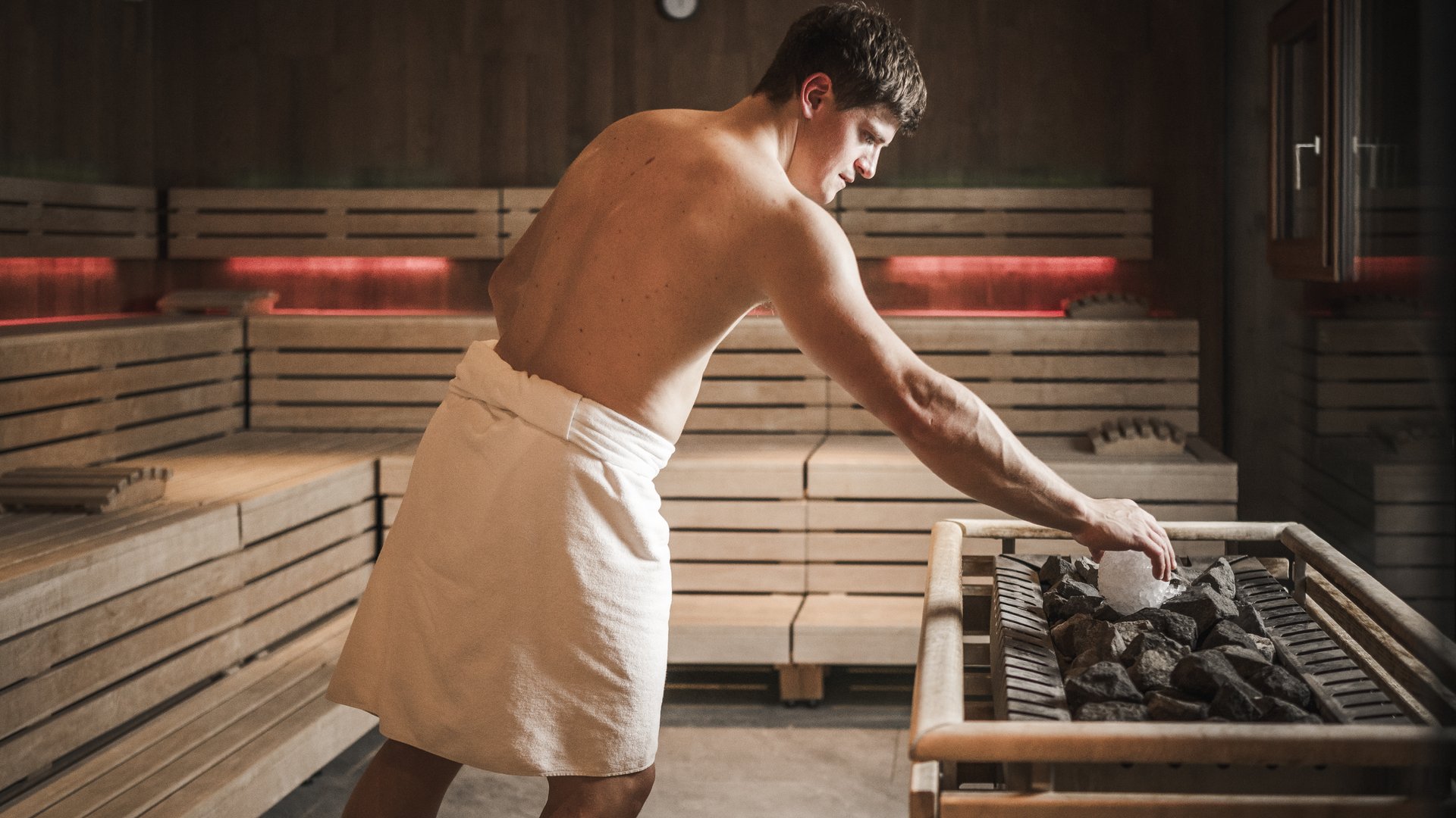 Belvita Leading Wellnesshotels Südtirol Mann in Sauna mit Handtuch gibt Eis auf heiße Steine