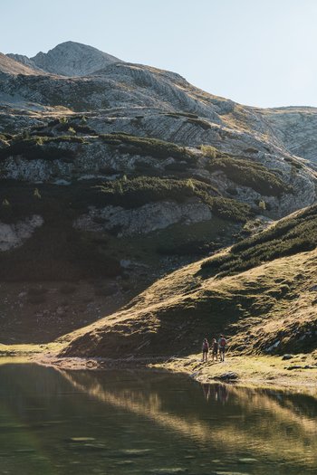 Excelsior: Wanderhotel in den Dolomiten Wanderer am Seeufer vor sonnenbeschienenen Bergen