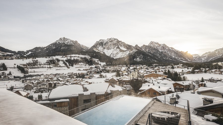 Hotel di lusso in Alto Adige: i nostri ospiti Paesaggio montano invernale con piscina esterna riscaldata e villaggio innevato