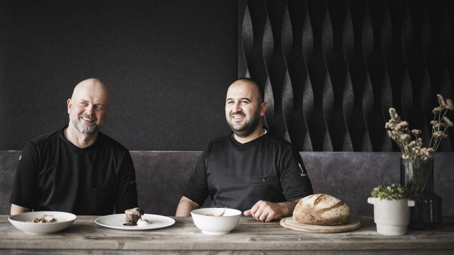 The gourmet hotel in South Tyrol Two men sitting at a table with various dishes and a loaf of bread