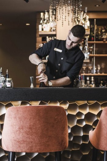 Il vostro hotel gourmet in Alto Adige Barista prepara una bevanda in un bar elegante con bancone illuminato decorativo