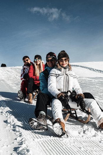 Il nostro hotel sulle piste a San Vigilio di Marebbe Quattro persone slittano insieme su una collina innevata con cielo sereno