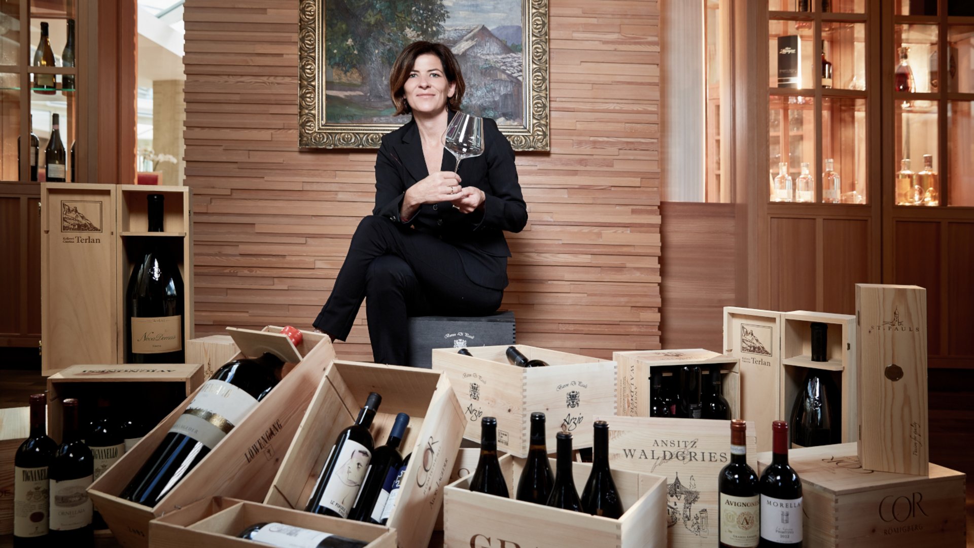 Wellnesshotel in den Dolomiten Frau sitzt umgeben von Weinflaschen und Holzkisten mit Wein in edlem Raum