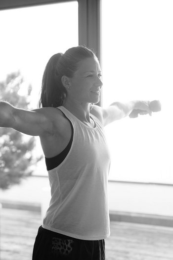 Your hotel in St. Vigil in Enneberg!! Woman doing lateral arm raises with dumbbells by large window