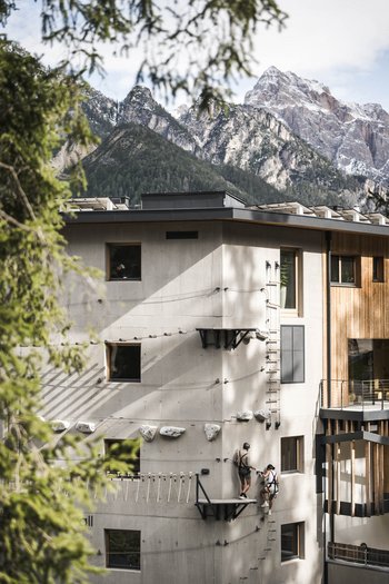 More than a hotel: Excelsior People climbing an artificial wall on a modern building with mountains in the background