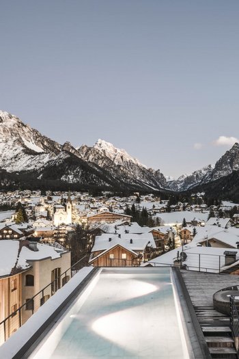 Wellnesshotel in Südtirol: Auf in den Traumurlaub! Schneebedecktes Dorf in den Bergen mit beleuchtetem Dorfzentrum bei Abenddämmerung