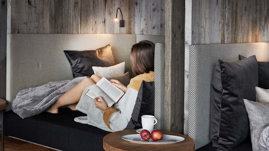 Wellnesshotel in den Dolomiten Frau entspannt auf Couch mit Buch und Obst auf Beistelltisch