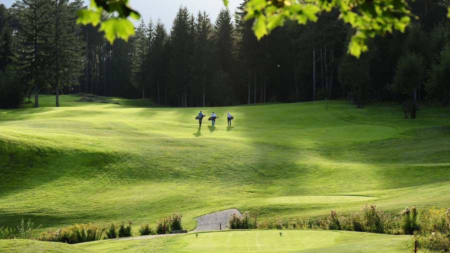 Il vostro hotel a San Vigilio di Marebbe con piscina Tre golfisti con mazze su campo da golf verde con bosco sullo sfondo