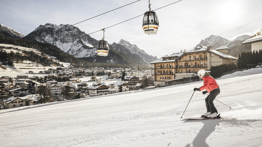 Hotel at Plan de Corones/Kronplatz on the slopes Skier descending slope with cable cars and village in background