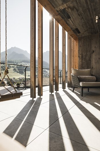 Wellnesshotel in den Dolomiten Terrasse mit Schaukel, Sesseln und Bergpanorama im Sonnenlicht