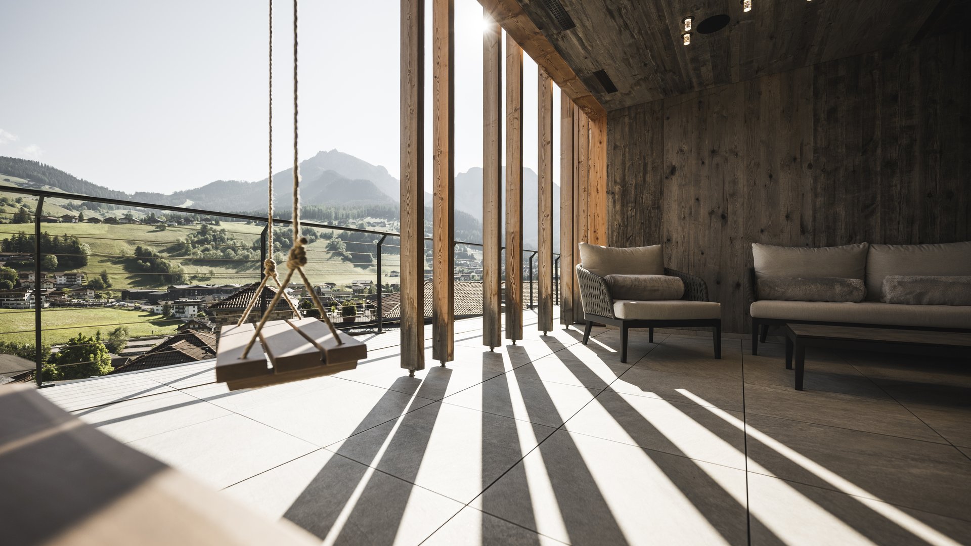 Hotel in the Dolomites for adults only Terrace with swing, armchairs, and mountain view in sunlight
