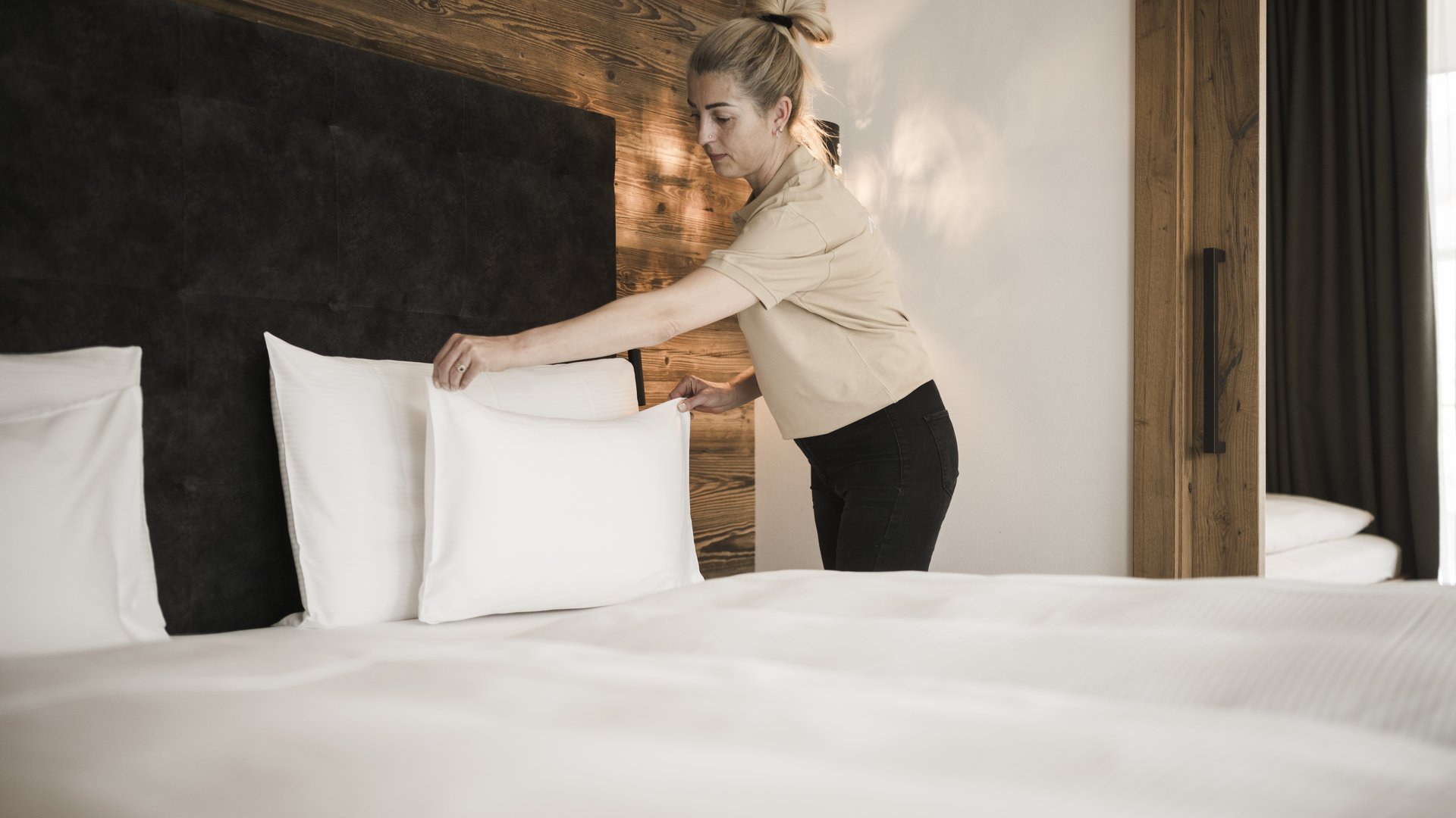 Wellness nel nostro hotel sulle Dolomiti: schiena al top Donna sistema il letto con cuscini bianchi in una camera da letto