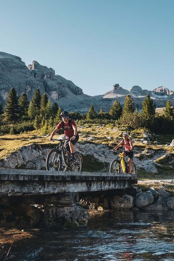 Bike offers and impressions Two mountain bikers crossing a bridge in the mountains on a sunny day