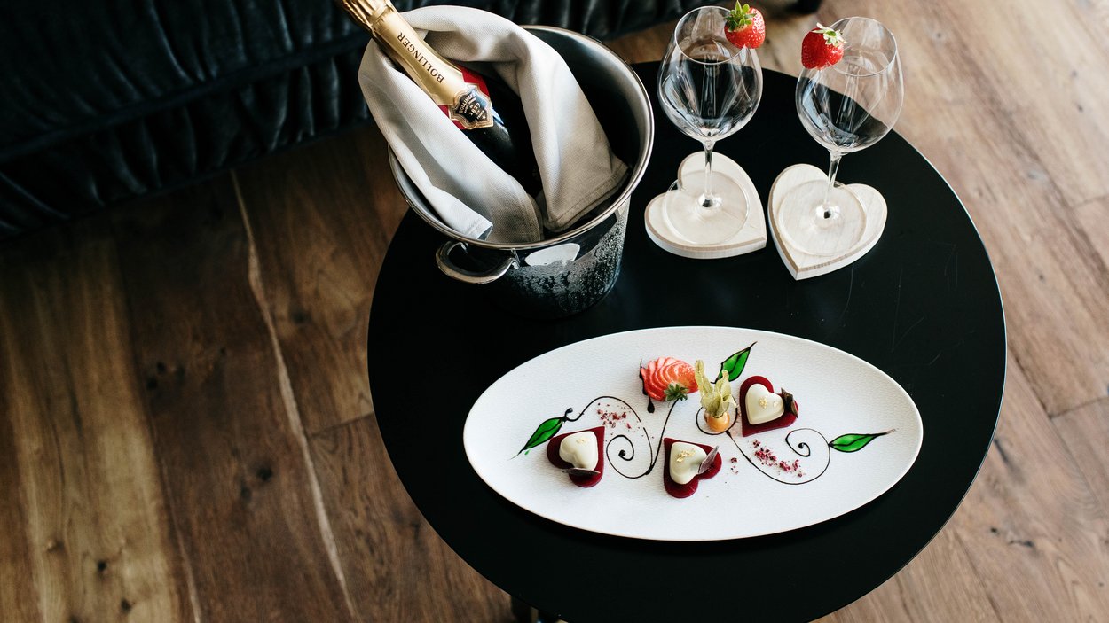 #myexcelsior Sunday News 09.02.2025 Sektflasche im Eiskübel, zwei Gläser mit Erdbeeren und dekorierte Dessertplatte auf rundem Tisch