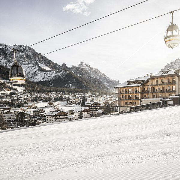 Dolomiten-Hotel für Bergmenschen Seilbahnkabinen über einem verschneiten Skiort mit Bergen im Hintergrund