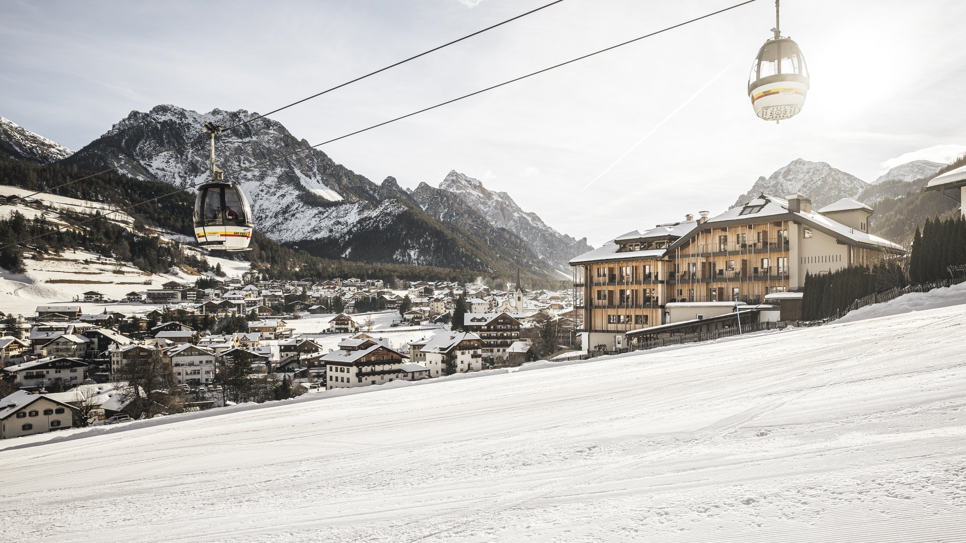 Ihr Hotel in St. Vigil in Enneberg! Seilbahnkabinen über einem verschneiten Skiort mit Bergen im Hintergrund