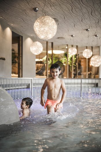 Familienurlaub in den Dolomiten – Natur, Erholung & Abenteuer Kinder spielen und planschen in einem beleuchteten Hallenbad