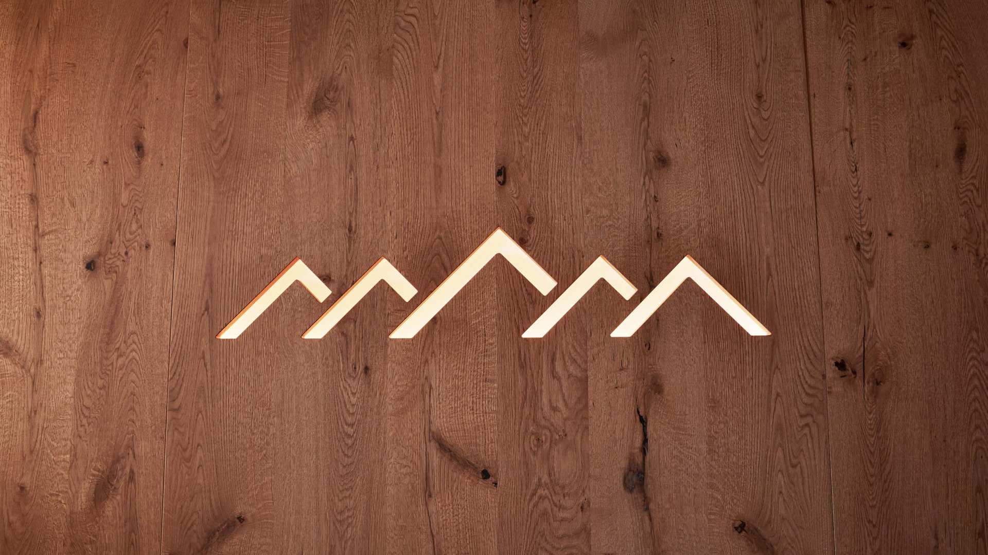 Info on our hotel in St. Vigil in South Tyrol Wooden wall with illuminated abstract mountain symbol