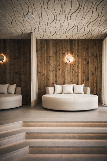 Hotel con infinity pool in Alto Adige: l’Excelsior Divano rotondo con cuscini bianchi davanti a parete in legno in stanza moderna