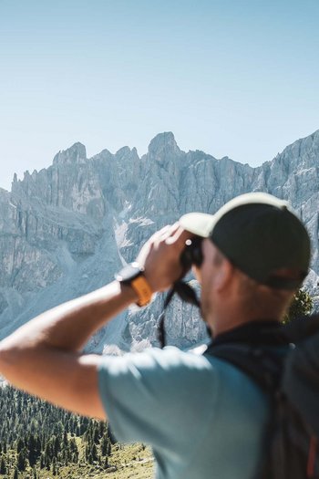 Il vostro hotel a San Vigilio di Marebbe con piscina Escursionista con binocolo osserva catena montuosa rocciosa