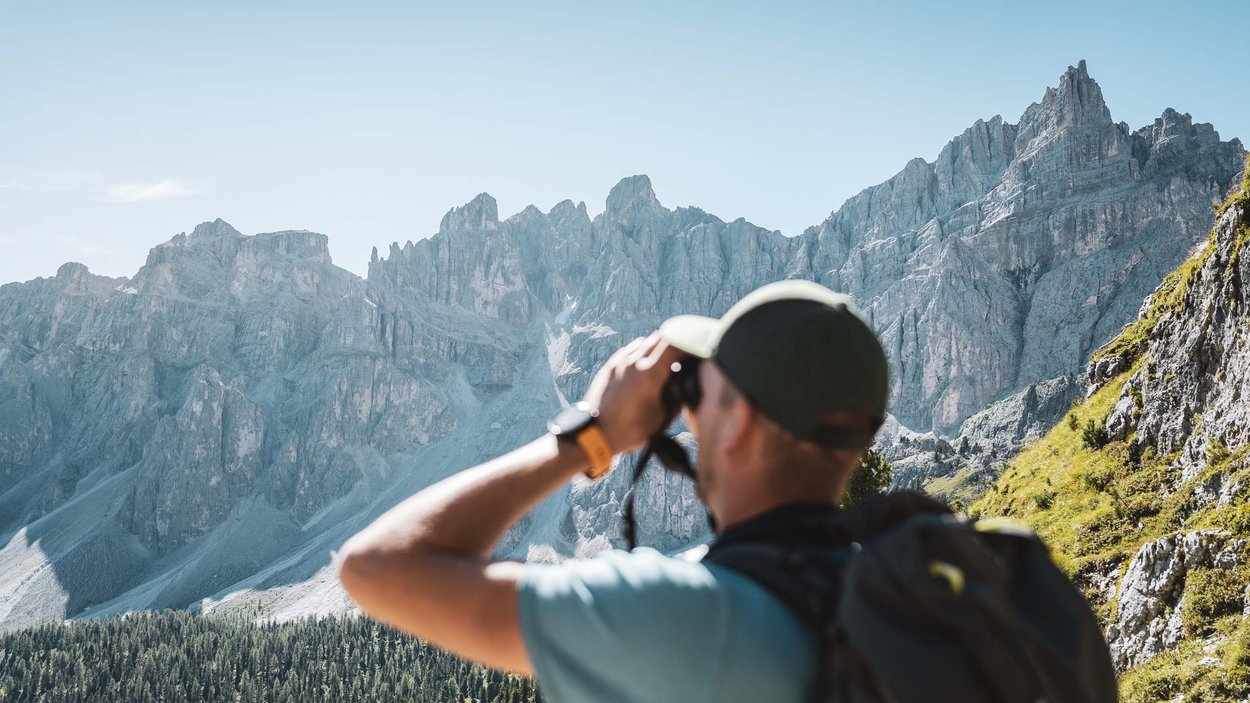 Excelsior: Wanderhotel in den Dolomiten Wanderer mit Fernglas blickt auf felsige Berglandschaft