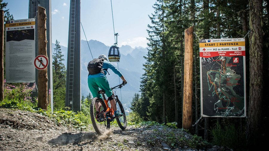 Regione bike Mountain biker inizia il trail Piz de Plaies nella foresta con cabinovia sullo sfondo