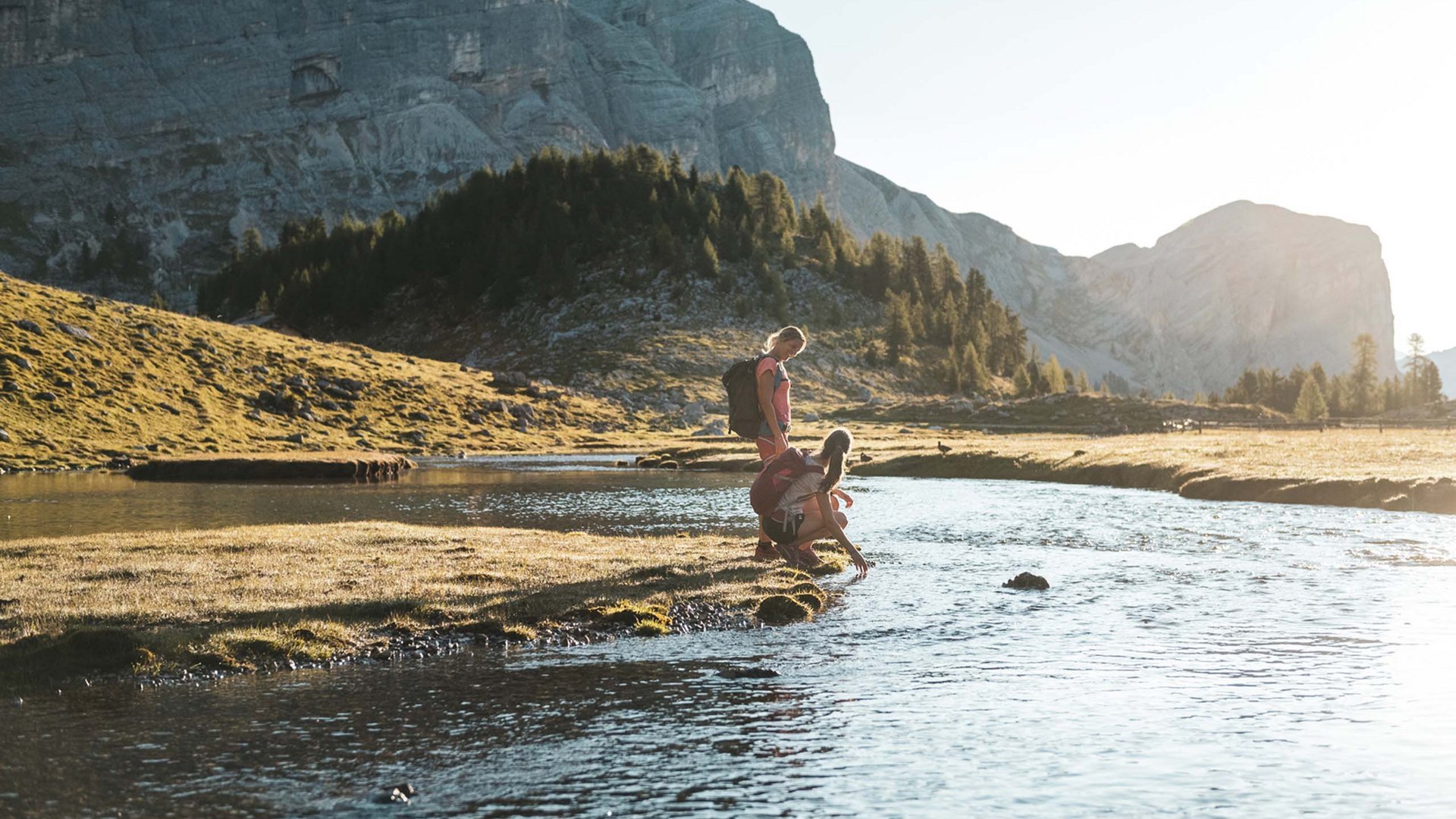 Wanderhotels Südtirol in the Dolomites Two hikers by a mountain river at sunset