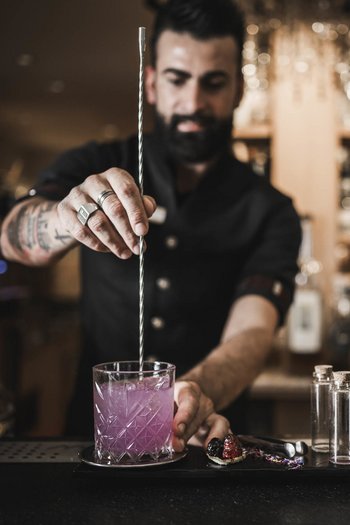 Das Gourmethotel in Südtirol Barkeeper rührt rosa Cocktail an der Bar mit dekoriertem Tablett