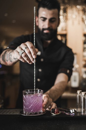 Il vostro hotel gourmet in Alto Adige Barista che mescola un cocktail rosa al bancone con vassoio decorato