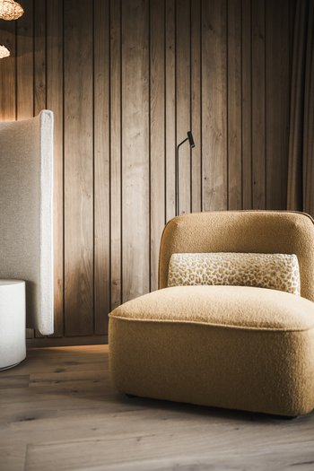 Le nostre novità 2024 Comoda poltrona gialla imbottita davanti a parete in legno