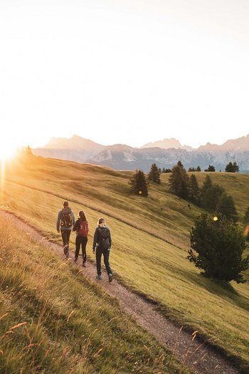 Il vostro hotel a San Vigilio di Marebbe con piscina Tre escursionisti su sentiero di montagna al tramonto con le Alpi sullo sfondo