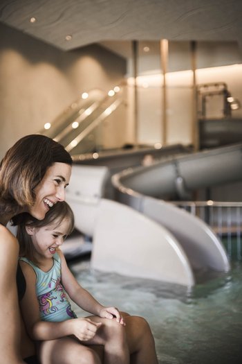 Excelsior: hotel wellness in Alto Adige per famiglie Madre e figlia ridono insieme accanto a una piscina con scivolo