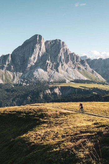 Excelsior: Wanderhotel in den Dolomiten Mountainbiker fährt auf einem Weg vor hohen Bergen bei klarem Himmel