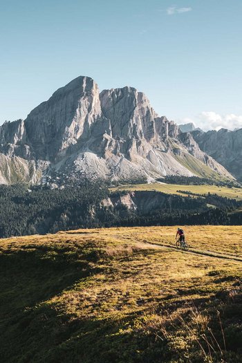 Wanderhotels Südtirol in the Dolomites Mountain biker riding on a trail in front of tall mountains under clear sky