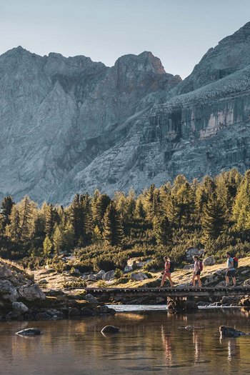 Hotel in South Tyrol with guided hikes Three hikers cross a bridge in the mountains at sunset light