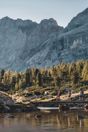 Excelsior: Wanderhotel in den Dolomiten Drei Wanderer überqueren eine Brücke in den Bergen bei Sonnenlicht