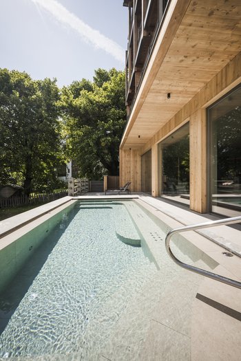 Family-friendly hotel in South Tyrol Modern wooden building beside clear pool with green trees surrounding it