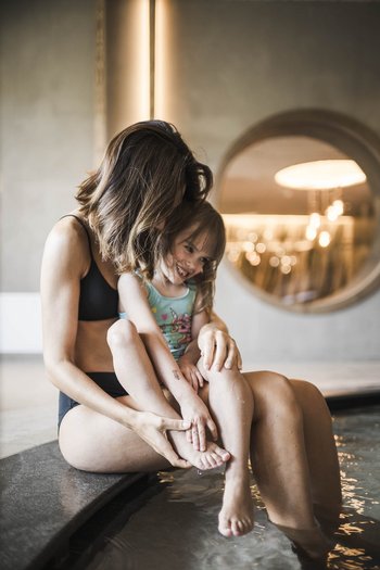Family-friendly hotel in South Tyrol Woman and child sitting by pool, woman holding smiling child in arms