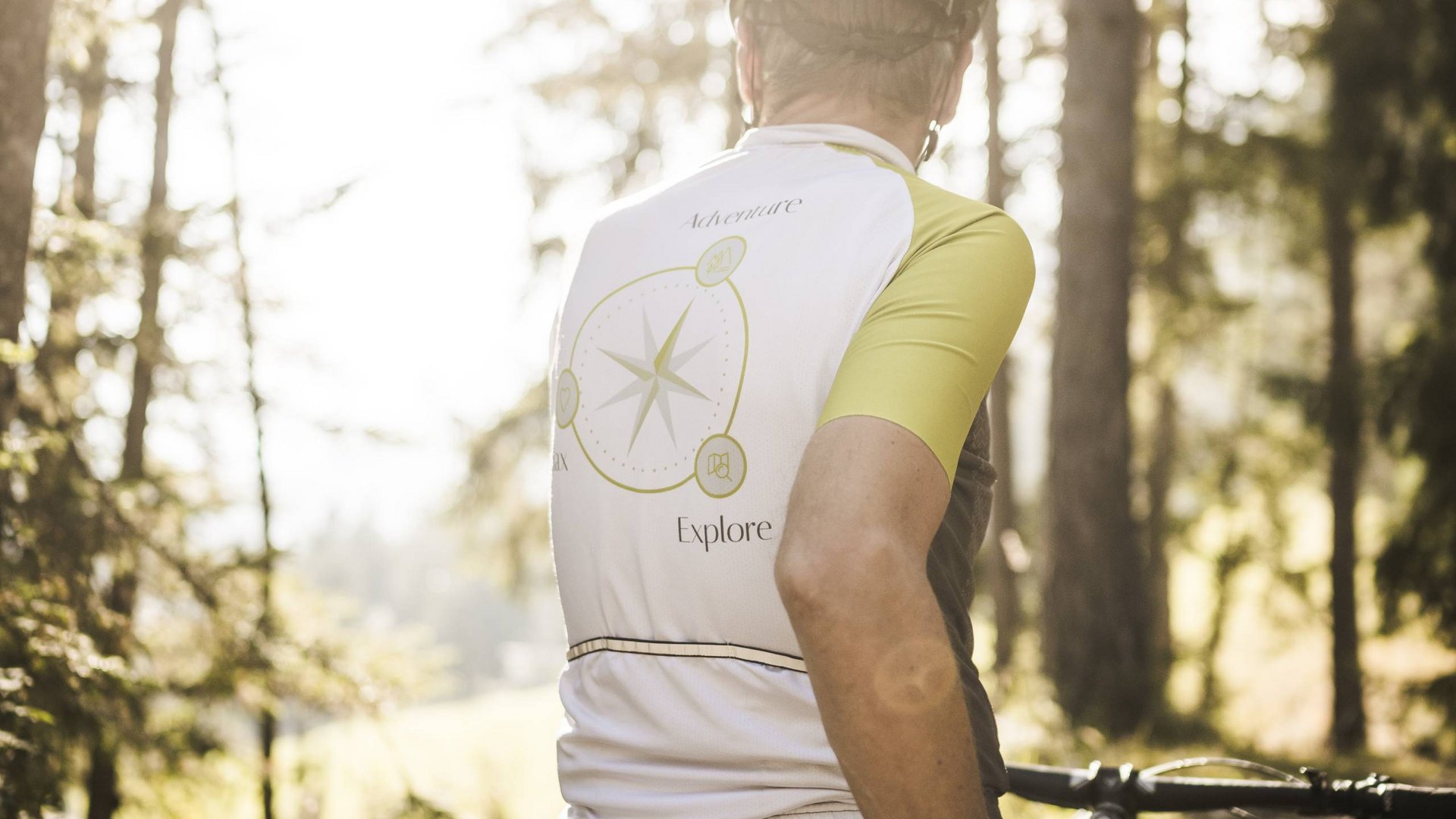 Bici gravel a San Vigilio Ciclista nella foresta con maglia bianca e gialla con disegno della bussola