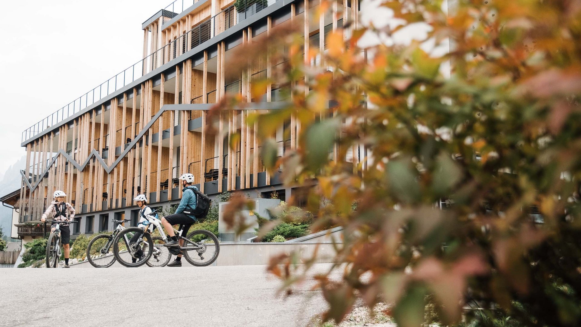 Bike-Verleih Drei Radfahrer mit Helmen vor modernem Gebäude mit Holzfassade