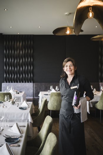 Il vostro hotel gourmet in Alto Adige Cameriera con bottiglia di vino in ristorante elegante con tavoli apparecchiati