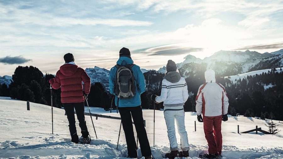 Hotel di lusso in Alto Adige: i nostri ospiti Quattro persone sulla neve che guardano le montagne innevate al tramonto