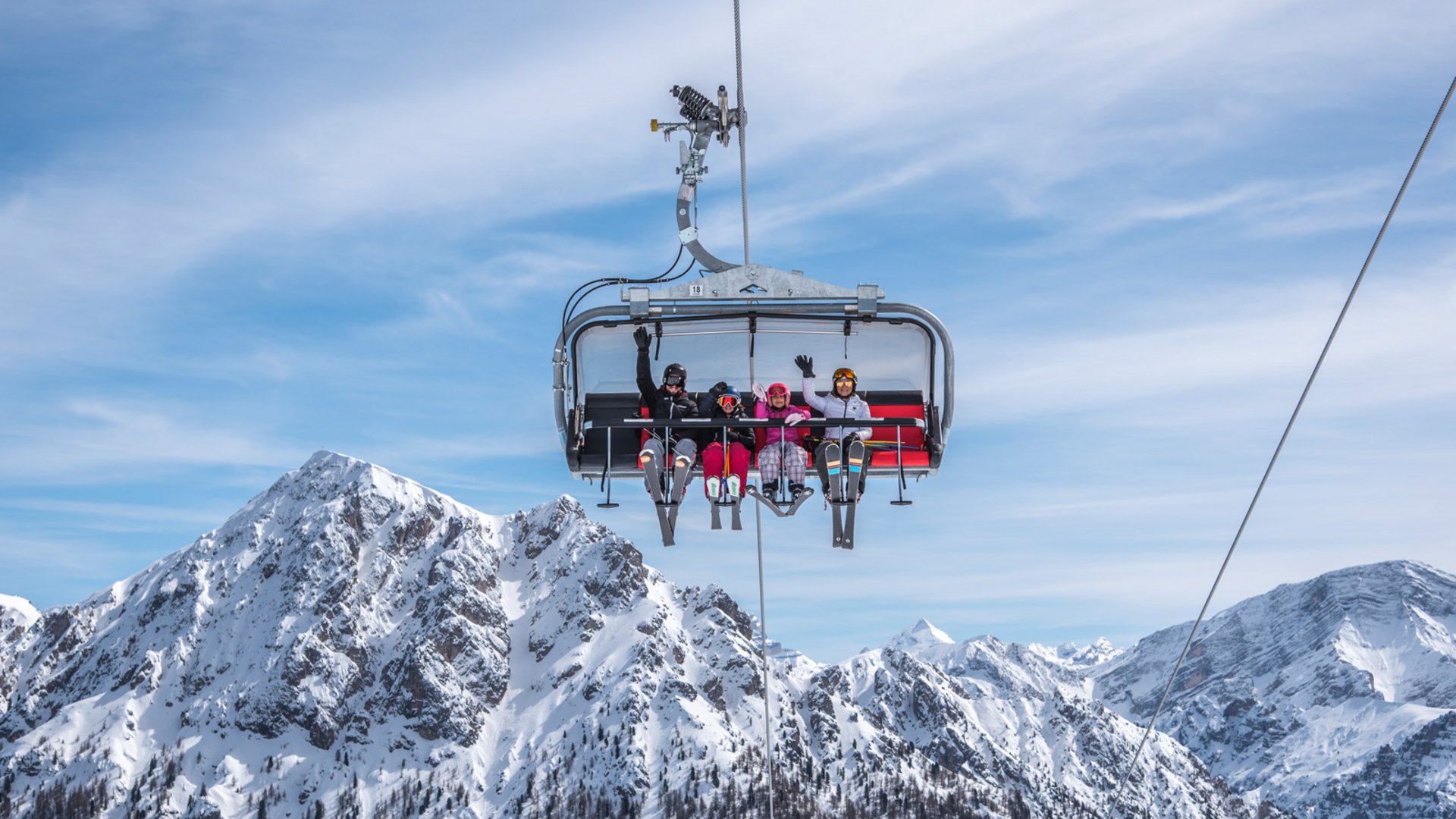 Around the hotel on the slopes in South Tyrol Four skiers waving on chairlift against snowy mountain peaks