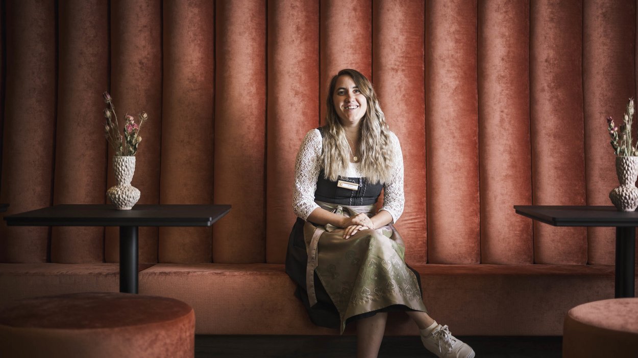 Sustainable hotels in South Tyrol? The Excelsior! Woman in traditional dress sitting on orange bench in modern setting