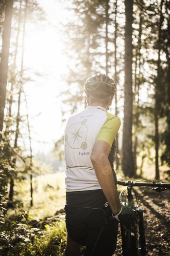 Hotel in South Tyrol with guided hikes Man with bike standing in forest looking towards the bright sun