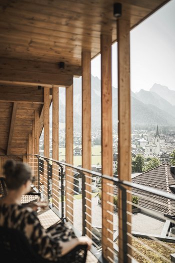 More than a hotel: Excelsior Person relaxing on balcony overlooking mountain village and church